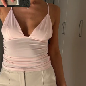 Ljusrosa urringad topp  - Säljer en ljusrosa linnetopp med smala axelband och djup v-ringning. Toppen har en tight passform och är tillverkad i ett mjukt, stretchigt material. Kolla mina andra annonser för billiga väskor & kläder 🤍