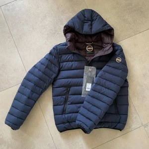 Colmar jacka helt ny marinblå vinröd - Snygg blå pufferjacka från Colmar med dragkedja och huva. Perfekt för våren med en lyxig vinröd interiör! Kvitto finns, helt oanvänd. Nypris 4 472kr 