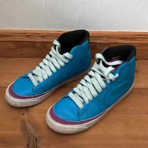 Höga Nike sneakers - Snygga blå Nike sneakers med högt skaft och vita snören. Skorna har en lila detalj runt sulan och svart insida. Använda endast ett fåtal gånger. 