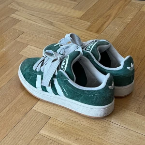 Gröna Adidas Campus sneakers - Snygga gröna Adidas Campus sneakers i grön mocka med vita detaljer och snörning. Perfekta för en avslappnad stil med klassisk design och bekväm passform. Slitage på insidan av vänster sko, se även bild 