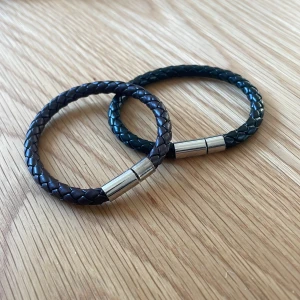 Flätade armband i läder - Helt nya flätade armband i läder, ett i svart och ett i brunt. Båda har ett praktiskt lås i silverfärgad metall. 