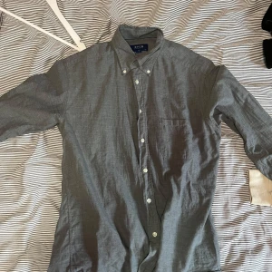 Grå skjorta från Eton - Säljer en stilren grå skjorta från Eton i storlek M. Skjortan har en klassisk design med knappar framtill och en bröstficka. Perfekt för en elegant look.