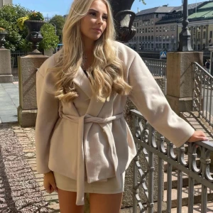 Beige kappa med bälte - Elegant beige kappa med bälte och långa ärmar. Perfekt för en stilren look, från missay.