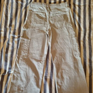 Randiga cargobyxor från H&M - Säljer ett par randiga jeans för dem inte passar längre. Dem har fyra  fickor på sidorna av byxorna och är perfekta färger nu till sommaren. Eftersom byxorna är ljusa så är de luftiga och sköna att ha på sig. 