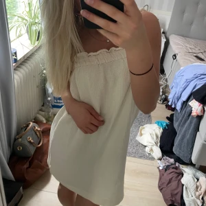 Beige kortklänning - Supersöt beige kortklänning med en smockad överdel. Klänningen har en lätt volangkant upptill och är gjord i ett luftigt, strukturerat bomullstyg. Perfekt för varma dagar och enkel att styla med smycken eller en jeansjacka. Kommer från hm och är i storlek XS.