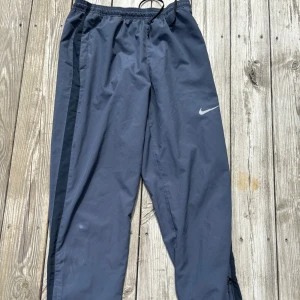 Träningsbyxa- Nike  - Mörkblåa byxor från Nike som passar till det mesta. Använts flertal gånger, finns slitage runt höger knä och ett hål (1•2mm). Fickorna har tryckknapp man stänger dem med.
