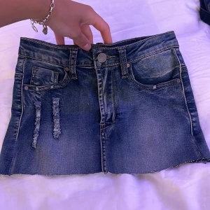 Mörkblå jeanskjol med slitningar - Snygg mörkblå kort jeanskjol med rå kant och slitna detaljer fram och bak. Den sitter bra där bak 