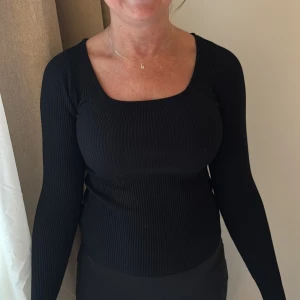 Svart ribbad långärmad tröja - Snygg svart långärmad tröja med ribbad struktur och fyrkantig ringning. Tröjan har en tight passform och är perfekt för dig som gillar en stilren och enkel look. Passar till både jeans och kjol.