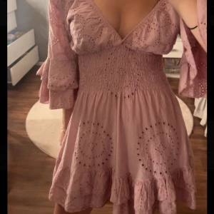 Söt rosa klänning🌸🌷🌺 - Supersöt rosa kortklänning med v-ringning, volangdetaljer och broderade mönster. Klänningen har trekvartsärm med volang och smockad midja som ger en snygg passform. Perfekt för sommaren! Säljer då den inte kommer  till användning. Köptes på en Spanien marknad🌸🌺🌷