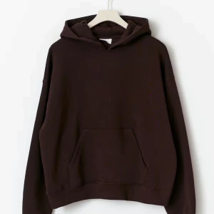 Mörkbrun hoodie med huva - Säljer en stilren mörkbrun hoodie med huva och stor magficka. Tröjan har en avslappnad passform och långa ärmar, perfekt för att chilla eller dra på sig till skolan. Enkel design utan tryck eller mönster.