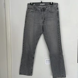 Grå loose fit jeans Jack & Jones - Grå jeans från Jack & Jones i loose fit-modell, modellen Chris. Klassisk femficksdesign, raka ben och normal midja. Jeansen är tillverkade i bomull och har en snygg tvättad look med metallknapp och nitar.