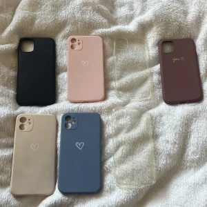 7 snygga mobilskal i olika färger - Säljer 7 mobilskal till iPhone 11 i olika färger: svart, beige, blå, rosa, vinröd och två genomskinliga. Några har hjärtmotiv eller texten 'You.' på baksidan. Skalen är i mjuk silikon och plast, perfekta för att ge mobilen en personlig touch. Skriv till mig om ni undrar något💕Man måste inte köpa alla utan kan köpa bara en eller kanske 2. Priset är för 1 mobilskal inte för alla💕 + frakt, priset kan diskuteras men jag säljer inte för något under 25kr 