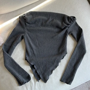 Mörkgrå ribbad långärmad tröja - Säljer en mörkgrå långärmad off-shoulder tröja med ribbat tyg och asymmetrisk, spetsig nederkant. Ganska liten i storleken skulle jag säga och rätt croppad på sidorna. Aldrig använd från Shein