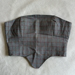 Rutig grå topp från Collusion - Säljer en croppad topp från Collusion i grått med rutor i rött och oranget. Toppen är axelbandslös och har hakknäppning bak. Helt oanvänd men saknar prislapparna