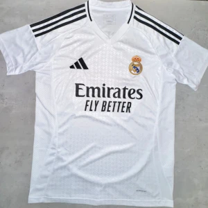 Real Madrid Hemmatröja 2023/24  - Madrid hemmatröja 2023/24 från Adidas! Stilren design med klubbens klassiska vita färg, broderad logo och “Emirates Fly Better”-tryck. Perfekt för fans eller som present. Storlek M, ny och oanvänd.