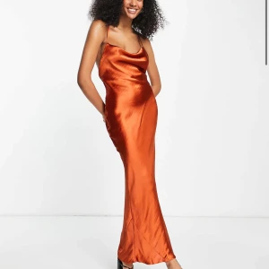 Lång orange satinklänning med snörning - Snygg långklänning i glansig orange satin med axelband och öppen rygg med snörningsdetalj. Klänningen har en figurnära passform och faller snyggt längs kroppen. Den sitter jätteskönt. SKRIV FÖR ATT SE FLER BILDER. Endast använd en gång. Originalpris: 800 kr