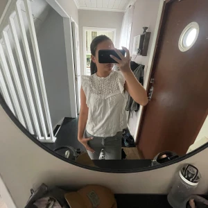 Vit blus med spets och volang - Supersöt vit blus med spetsdetaljer över bröstet och volang vid axlarna. Perfekt att styla med jeans eller kjol för en fräsch look.