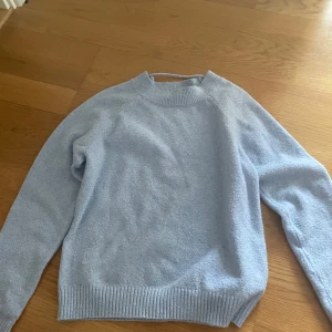 Ljusblå stickad tröja från Vero Moda - Supermysig ljusblå stickad tröja från Vero Moda. Tröjan har en klassisk rund halsringning, ribbade muddar och lång ärm. Perfekt för lager-på-lager och chill dagar. Enkel att matcha med jeans eller kjol för en clean look.