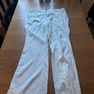 Vita linnebyxor med rak passform - Snygga vita linnebyxor med rak passform och klassisk look. Byxorna har sidfickor och bakfickor, perfekt för en chill och stilren vibe. Lätta och luftiga, perfekta för varmare dagar.