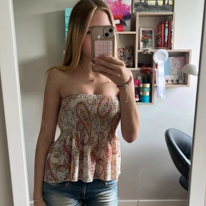 Beige kortkjol med paisleymönster - Supersöt kortkjol i beige med färgglatt paisleymönster. Kjolen har ett luftigt material, perfekt för när det är varmt. Kan användas som både topp och kjol 🧡