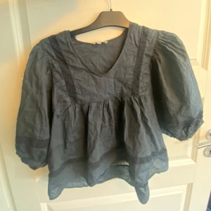 Marinblå blus med puffärm från lager 157 - Supersöt marinblå blus  i storlek XS. Blusen har puffiga trekvartsärmar, v-ringning och fina spetsdetaljer längs ärmar och nederkant. Den är luftig och har en lös passform med volang nedtill, perfekt för en trendig look. Inga defekter 