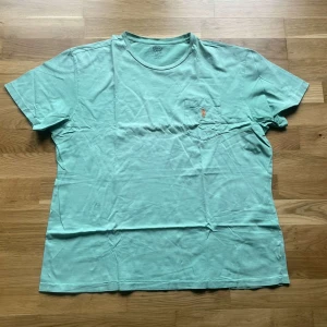 Ralph Lauren piké - Fräsch mintgrön t-shirt från Polo Ralph Lauren i 100% bomull. Klassisk passform med korta ärmar, rund hals och liten bröstficka med broderad logga i orange. Perfekt för dig som gillar stilrena och bekväma plagg. Pikén har ett antal skavanker som bland annat syns på sista bilderna och därav priset :)