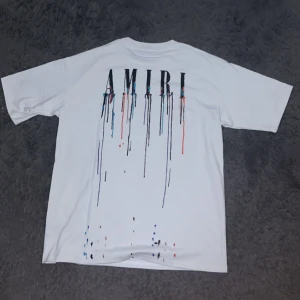Vit AMIRI t-shirt med färgstänk - Denna sprillans nya t-shirten från AMIRI med tryck av droppande färg och färgstänk både fram och bak, säljs pågrund av problem med passformen. Tröjan är en regular fit och tillverkad i mjuk bomull, denna t-shirt är perfekt för dig som vill sticka ut men ändå se bra ut.                                   Priset kan diskuteras!