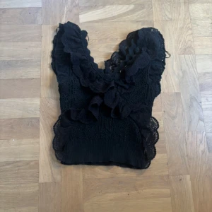 Svart volang topp med spets❤️ - Supersnygg svart topp med volanger och spetsdetaljer. Djup v-ringning och ärmlös design ger en trendig look. Perfekt att styla med jeans eller kjol för en cool outfit.🫶🏼