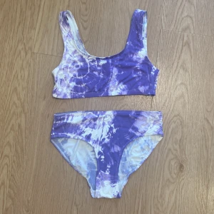 Lila och vit tie-dye bikini från Lindex storlek 158/164 - Superfin bikini från Lindex i lila och vitt tie-dye mönster. Tillverkad i återvunnen polyamidblandning, perfekt för strand eller poolhäng i sommar. Endast provat, aldrig använd.