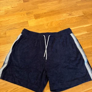 Mörkblå frottéshorts Calvin Klein - Mörkblå shorts från Calvin Klein i mjuk frotté med vita snören i midjan och logoband längs sidorna. Perfekta för sommaren med relaxed fit och sportig vibe. Snygga detaljer och bekväm passform gör dem till ett måste i garderoben.