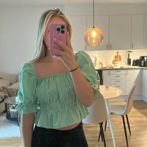 Blus med puffärmar - Grön och vit rutig blus med croppad passform, puffiga trekvartsärmar och volang nertill. Smockad midja och ärmar med knytband.  