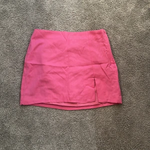 Rosa kortkjol med slits - En snygg rosa kortkjol med enkel design och en liten slits framtill. Kjolen har rak passform och är perfekt för dig som vill ha en färgklick i garderoben. Passar till många olika stilar och är lätt att matcha med både sneakers och boots.