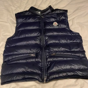 Mörk marin blå dunväst från Moncler - Snygg mörk marin blå dunväst från Moncler med dragkedja och två fickor framtill. Perfekt väst för alla dagar på året ( tycker jag ) . Västen har en quiltad design och Moncler-logga på bröstet. Storleken är small/1
