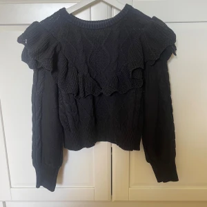Svart stickad tröja med volangdetaljer - Snygg svart stickad tröja med volangdetaljer på axlarna och över bröstet. Så fin och kan matchas till allt❣️❣️