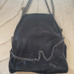 Svart axelväska med kedjedetaljer - Snygg svart axelväska som är mycket rymlig. Tyvärr har jag glömt tuggummi i den lilla ytterfickan som finns men det är inget som påverkar väskans användning inuti❤️