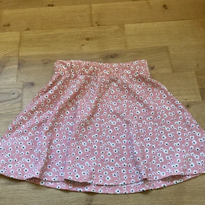 Rosa blommig kjol - Söt rosa kjol med blommigt mönster. Kjolen har en elastisk midja för bekväm passform. Perfekt för en varm sommardag  Köpt från lager 157 Storlek 140. Knappt använd 