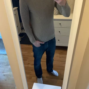 Beige stickad tröja från East West - Säljer en stilren beige stickad tröja från East West. Tröjan har långa ärmar och ribbade muddar vid ärmslut.