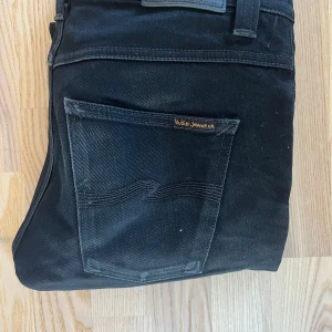 Svarta jeans från Nudie Jeans - Snygga svarta jeans från Nudie Jeans med en klassisk design. De har en snygg passform och är tillverkade i slitstarkt denim. Perfekta för en stilren look.