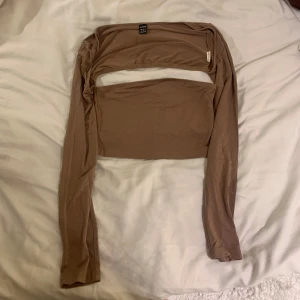 Beige axelbandslös bandeau topp 2 delar med bolero  - Säljer en beige topp med tillhörande  del med långa ärmar. Perfekt för en stilren och modern look. Aldrig använd 