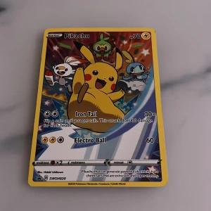 Pokémonkort Pikachu - (Psi 8) Säljer ett Pokémonkort med Pikachu som har attackerna Iron Tail och Electro Ball. Kortet har en färgglad design med flera Pokémon i bakgrunden och är märkt med SWSH020. Perfekt för samlare eller Pokémon-fans!