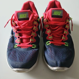 Nike Lunarglide 5 löparskor - Säljer ett par Nike Lunarglide 5 löparskor i en snygg kombination av mörkblått och rosa med gröna detaljer. Skorna har snörning och en bekväm sula för optimal dämpning. Perfekta för löpning och träning.