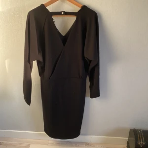 Svart klänning från b.young - Elegant svart klänning från b.young med v-ringning och öppen rygg. Klänningen har långa ärmar och en stilren design som passar perfekt för festliga tillfällen. Den är tillverkad i ett mjukt och bekvämt material. Ny och oanvänd i stl M
