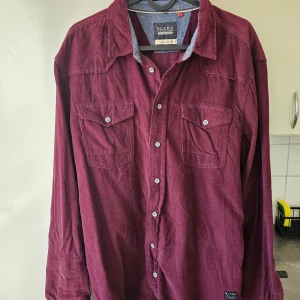 Vinröd skjorta från Blend - Snygg vinröd skjorta från Blend med klassisk krage och knappar framtill. Skjortan har två bröstfickor med knappstängning och är tillverkad i ett mjukt material. Perfekt för en stilren look.