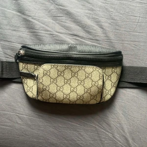Gucci Eden belt bag - Snygg midjeväska från Gucci med det klassiska GG-mönstret i beige och svart. Väskan har flera dragkedjeförsedda fack och en justerbar rem för bekväm passform. Perfekt för att hålla dina saker säkra och stiliga. Väskan är äkta 