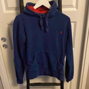 Blå hoodie från Ralph Lauren - Tja! Säljer en snygg blå hoodie från Ralph Lauren med röd logga på bröstet. Perfekt för en avslappnad stil. Storlek M. Den är använd några gånger men det finns inget fel med tröjan! Den är så gott som ny! Det står att den är storlek M fast den är väldigt liten i storleken! Skulle säga att den är mer som S eller XS!  