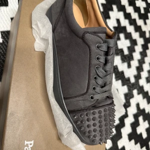 Grå sneakers med nitar från Christian Louboutin - Snygga grå sneakers från Christian Louboutin med coola nitar på tån. Skorna har snörning och är tillverkade i ett stilrent material som ger en lyxig känsla. Perfekta för att ge din outfit en edgy touch. 42 passar 43 med, kan även lösa fri frakt 
