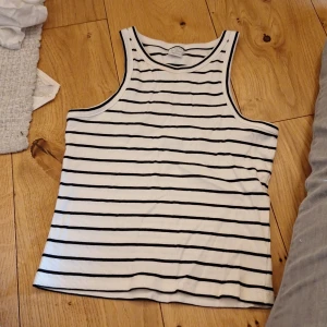 Linne - Säljer en snygg vit och svart randig linnetopp från Lindex. Perfekt för varma dagar med sin ärmlösa design och ribbade material. Passar både till jeans och shorts för en avslappnad look.