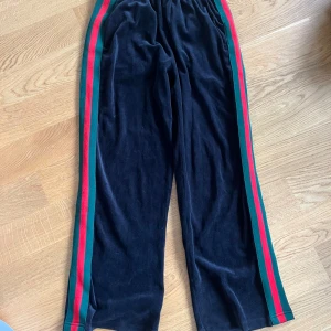 Svarta mjukisbyxor med ränder - Säljer ett par svarta mjukisbyxor med elastisk midja och färgglada ränder i rött och grönt längs sidorna. Inköpta i lokal butik i Manchester.  Sköna, använda ett par gånger. 