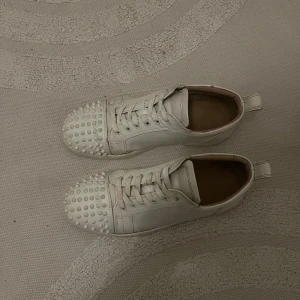 Vita sneakers med nitar från Christian Louboutin - Snygga vita sneakers från Christian Louboutin med coola nitar på tån. Skorna har snörning och en klassisk rund tå. Perfekta för att ge din outfit en edgy touch. Skorna passar även 43. Pris kan diskuteras! Billiga priset, pga väl använda.