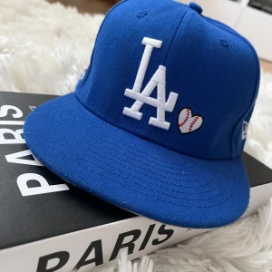 Blå La keps - Snygg blå keps från New Era med vit broderad logga och ett hjärta med basebollmönster. Använd ungefär 8 gånger och den är i storlek 7 1/8 (56,8 cm). Hör av er för funderingar.